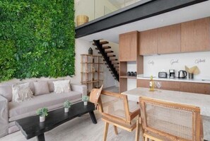 Ein moderner Wohnraum mit einer grünen Wand, einem Sofa, einem Esstisch mit Stühlen und einer Küchenzeile mit Holdekor und Arbeitsplatte.