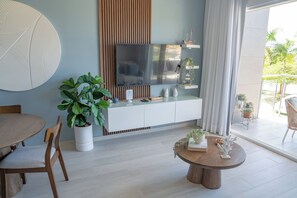 Ein modernes Wohnzimmer mit einem an der Wand befestigten Flachbildfernseher, einem Holzessttisch, einer Topfpflanze und einem runden Couchtisch.
