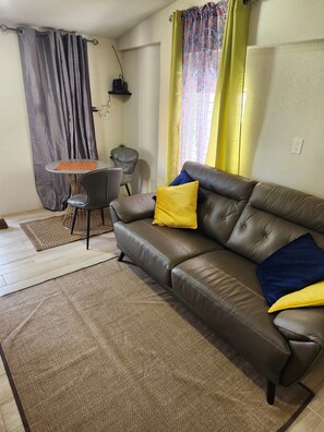 Ein Wohnzimmer mit einem braunen Ledersofa, einem kleinen runden Tisch, einem grauen Sessel und einem Teppich mit Muster.
