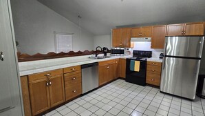 A kitchen with wooden cabinets, a stainless steel refrigerator, a microwave, and a dishwasher. - Prime Location Condo – Walk to Dining, Park, Shops & Downtown (Coleman)