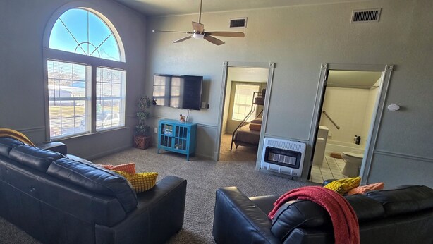 A living room with a large arched window, a ceiling fan, a fireplace, and a TV mounted on the wall. - Prime Location Condo – Walk to Dining, Park, Shops & Downtown (Coleman)