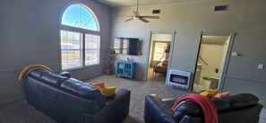 A living room with a large arched window, a ceiling fan, a fireplace, and a TV mounted on the wall.
