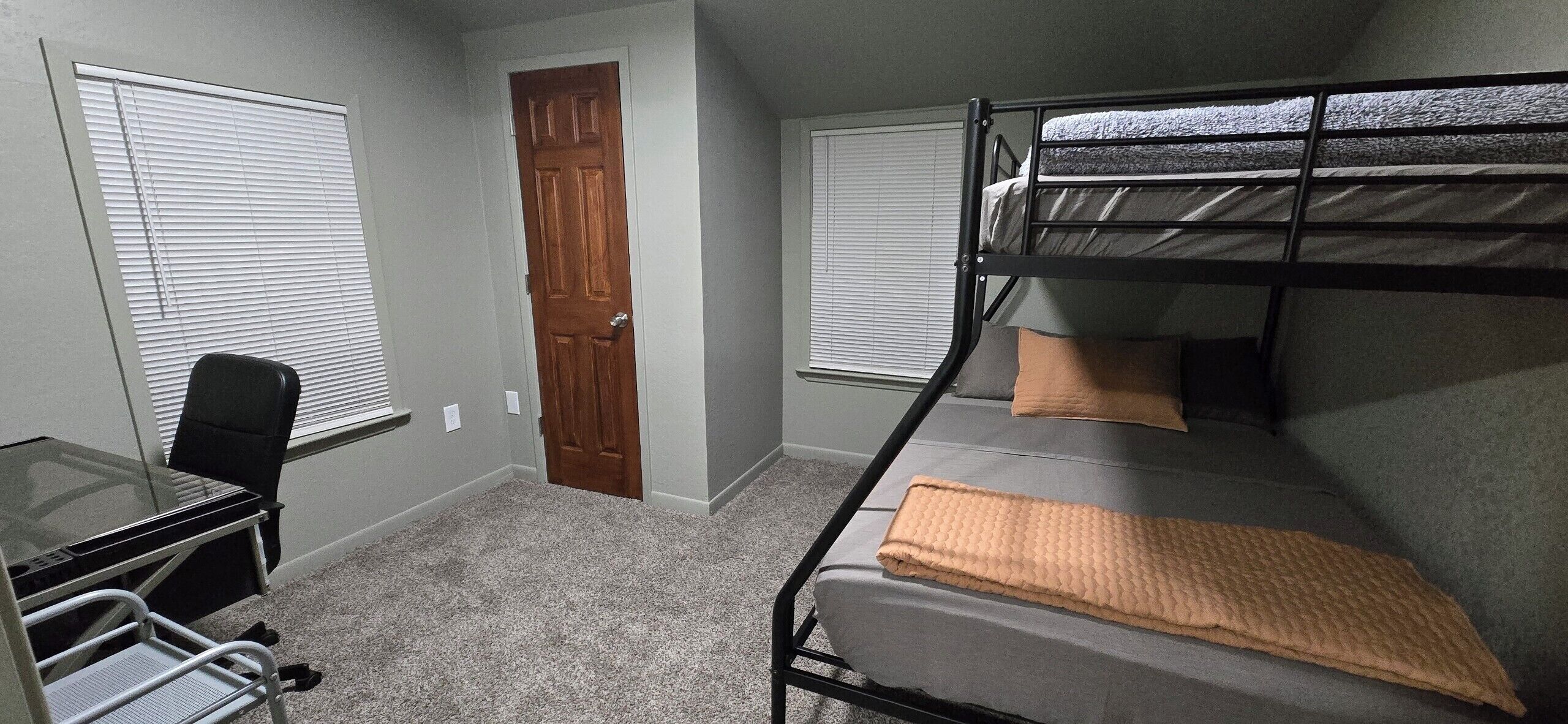 A room with a bunk bed, a desk with a chair, and a door.