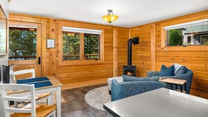 Interior acogedor de una cabaña con paredes de madera, una chimenea, una mesa de comedor con sillas y un sofá con cojines.