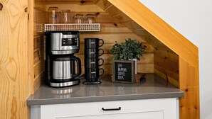 Una cocina con cafetera, un espacio para colgar tazas de café y una planta en maceta.