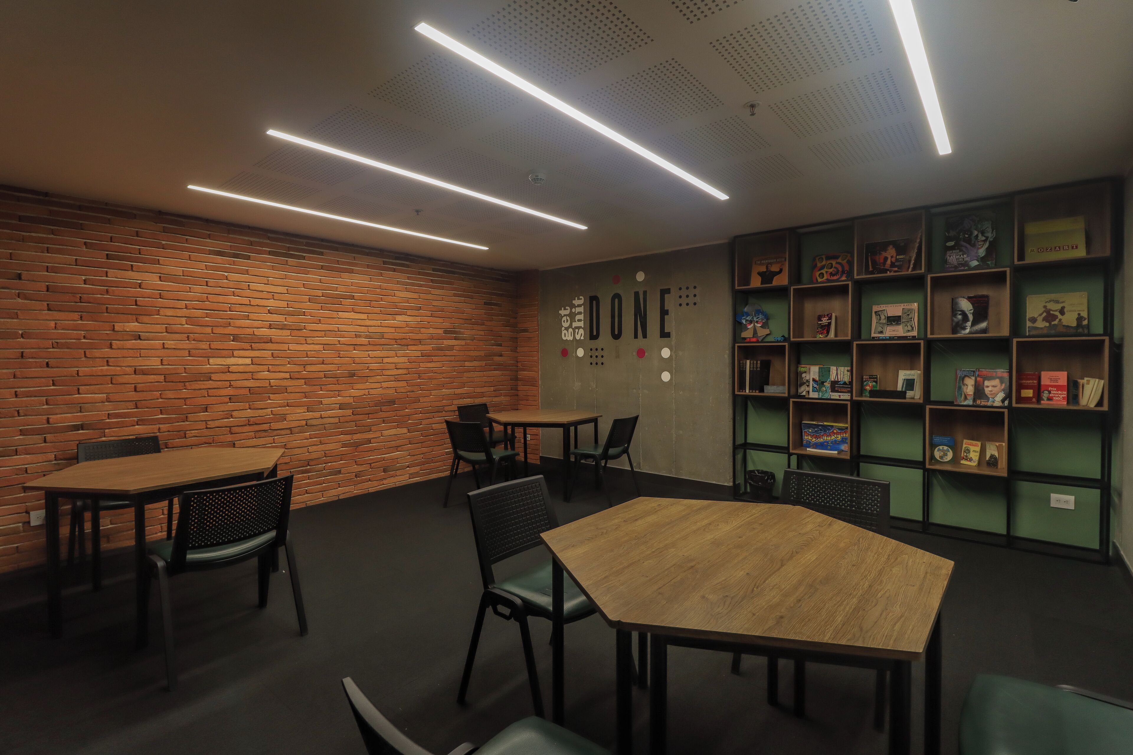 A modern meeting room with brick walls, a wooden table, and chairs. There are shelves with books and decorative items on the wall.