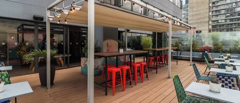 An outdoor seating area with tables and chairs, a covered section, and a view of a building in the background.