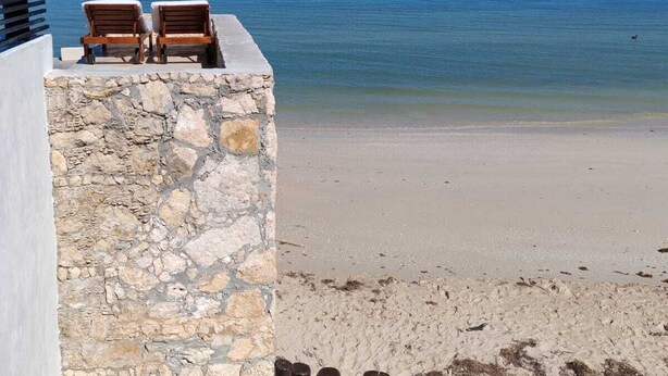 Un mur de pierre avec deux fauteuils en bois donnant sur l’océan.