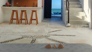 Une cuisine moderne avec des tabourets en bois, un escalier menant à un balcon donnant sur la mer et un toit de chaume.