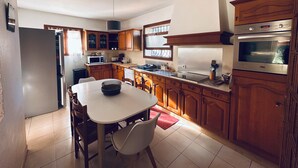 Een keuken met houten kastjes, een wit aanrechtblad, een inbouwoven en een eethoek met een tafel en stoelen.