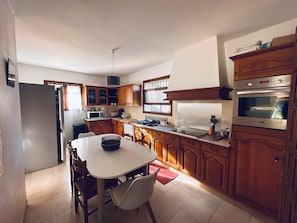 A kitchen with wooden cabinets, a white countertop, a built-in oven, and a dining area with a table and chairs. - Villa with private pool near Palombaggia (splendid beach) & Santa Giulia (porto vecchio)