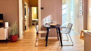 A hotel room with a wooden floor, a dining table with chairs, a potted plant, and a bed in the background. - Residenza Della Bollente II - Stylish cosy apartment in the heart of the town. (Acqui Terme)