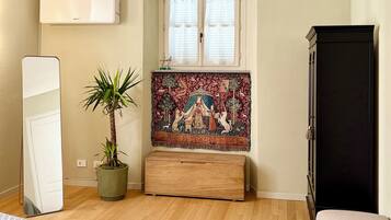 Une chambre à coucher avec un lit, une plante en pot, une tapisserie, une armoire et une fenêtre avec des rideaux.