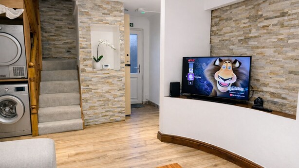 A modern hotel room with a stone wall, a flat-screen TV, a washing machine, and a staircase. - Peaceful 4-bedroom house in quaint stevenage perfect for families & contractors (Stevenage)