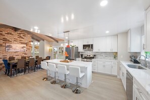 Una cocina moderna con armarios blancos, una isla central con taburetes de bar y una pared decorativa de ladrillo.