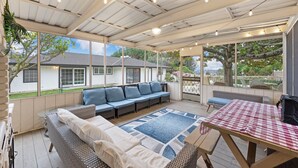 Un espacio de estar al aire libre cubierto con un sofá, una mesa y vistas a una casa y árboles.