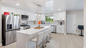 Una cocina moderna con armarios blancos, electrodomésticos de acero inoxidable y una isla central con taburetes de bar.