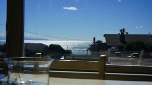 Vista desde una ventana hacia una playa con una casa y palmeras.