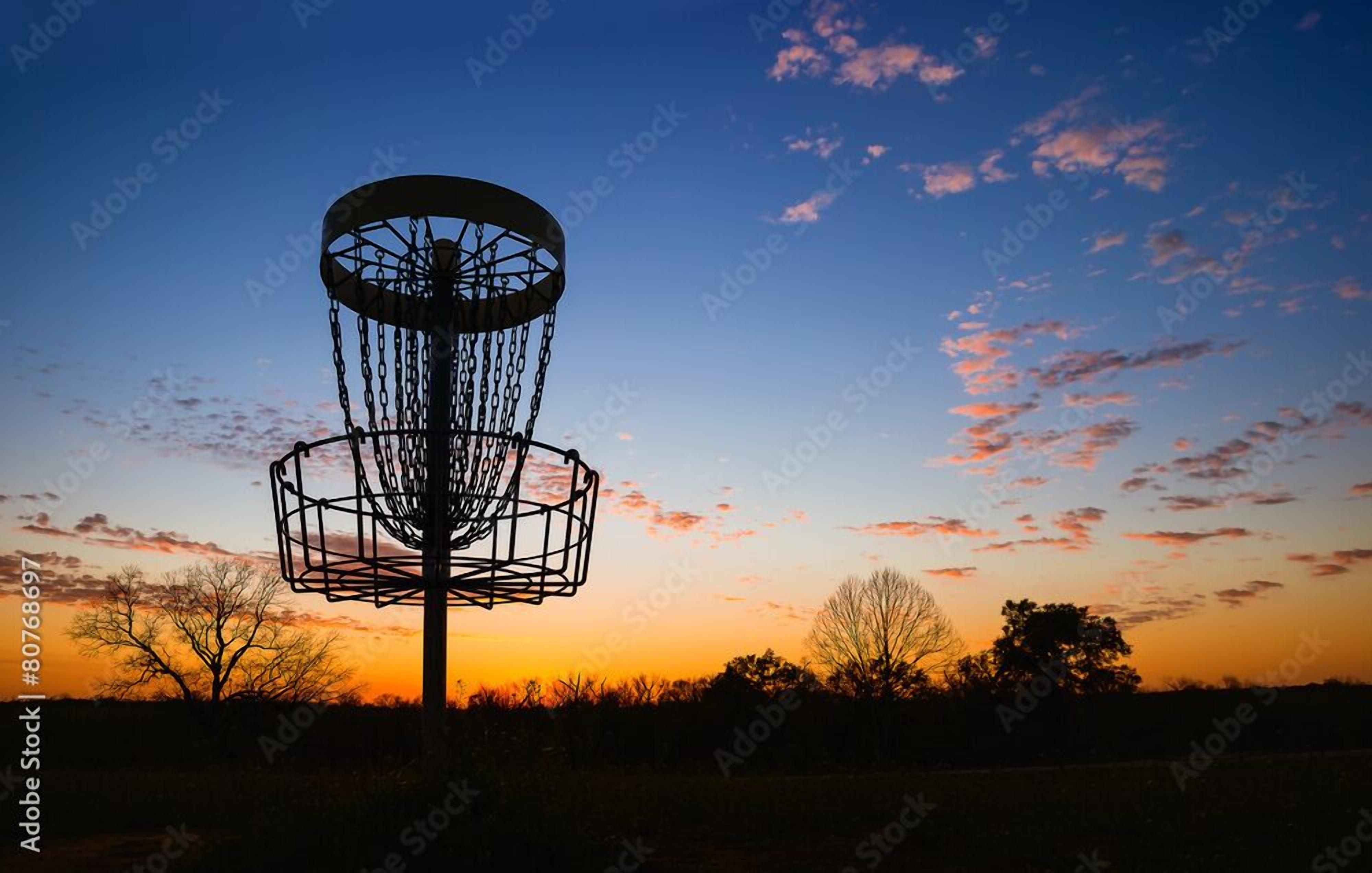 A disc golf basket against a sunset sky.