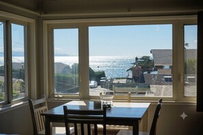 A dining area with a table and chairs, large windows with a view of the ocean and buildings. - East Cliff Nook (Santa Cruz)