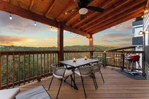 Um deck de madeira com mesa, cadeiras, churrasqueira e vista para a paisagem.