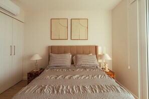 A bedroom with a bed, two bedside tables with lamps, a wardrobe, and two wall-mounted abstract art pieces. - Golden Light Beachfront Condo in the Heart of Town (Jaco)
