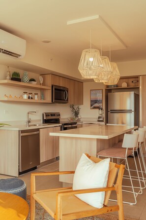 A modern kitchen with a central island, stainless steel appliances, and pendant lighting. - Golden Light Beachfront Condo in the Heart of Town (Jaco)