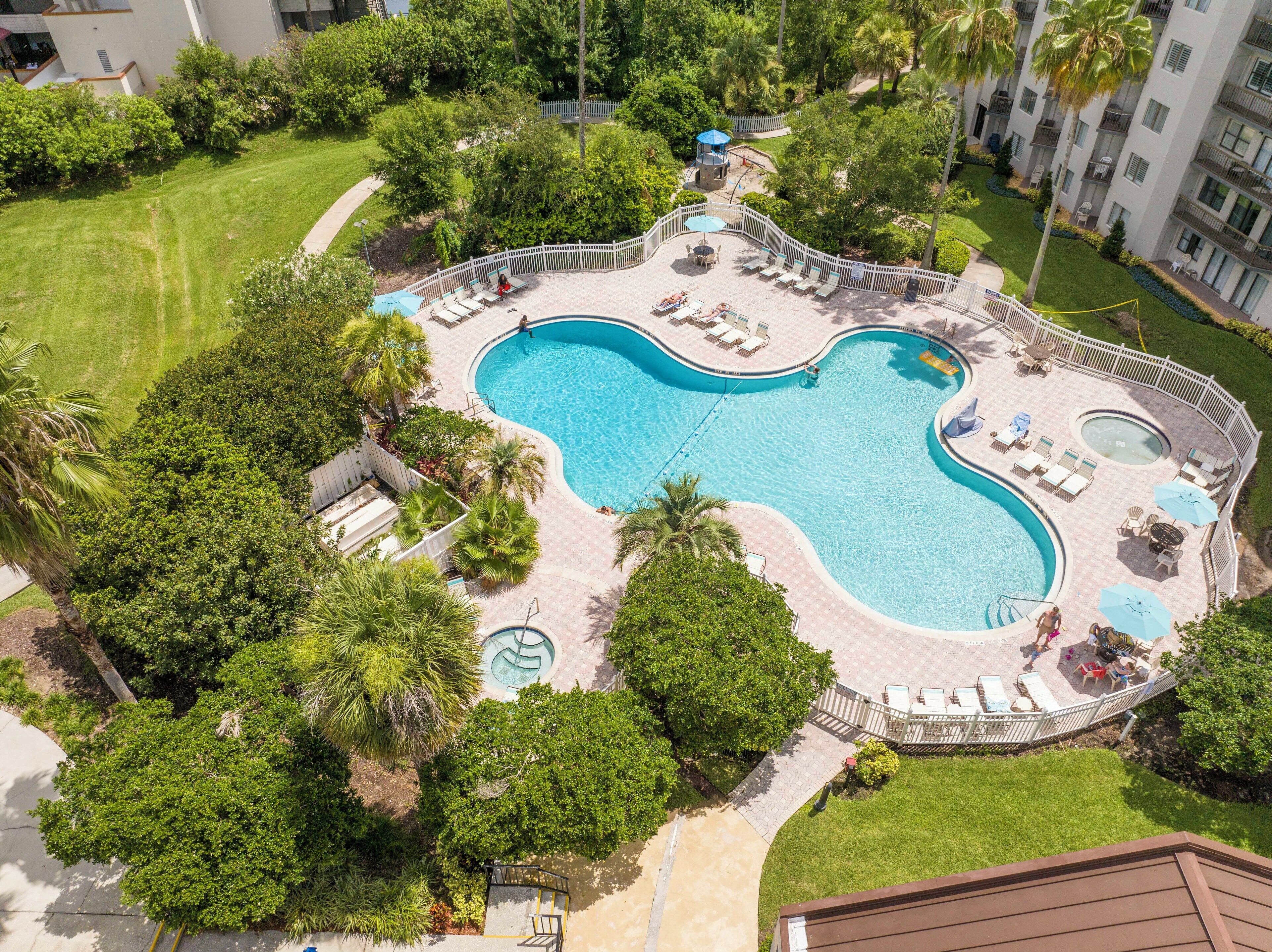 An aerial view of a resort with a large swimming pool surrounded by palm trees and lounge areas.