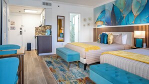 Une chambre d’hôtel moderne dotée d’un grand lit, de deux tables de chevet, d’un coin salon avec un banc et d’une fresque murale abstraite aux couleurs vives.