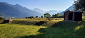 A rustic stone building with a wooden structure nearby, set against a backdrop of mountains and a grassy field. - Semi-detached chalet with breathtaking valley views (Saint-Léger-les-Mélèzes)