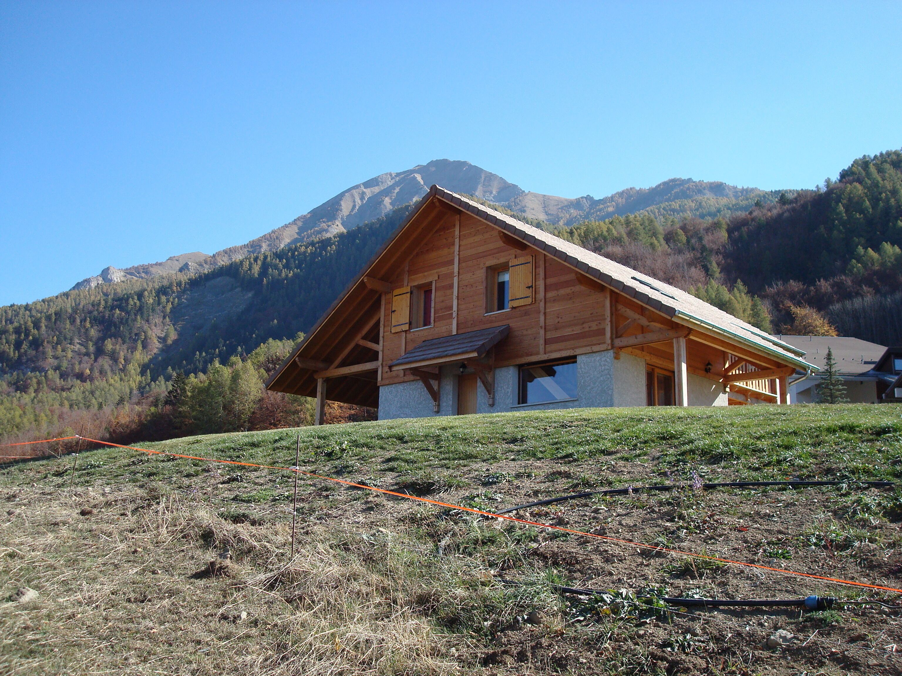 A wooden chalet with a sloped roof, set against a mountainous backdrop.