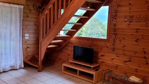 Ein Holzinnenraum mit einem Fernseher auf einem Schrank, einer Treppe und einem Fenster mit Blick auf Bäume.