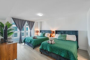 Moderni hotellihuone, jossa on kaksi sänkyä, televisio puupöydällä ja parveke, jossa on verhot.