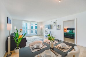 Un salon moderne comprenant un coin repas, un canapé, un téléviseur et un balcon offrant une vue sur la ville.
