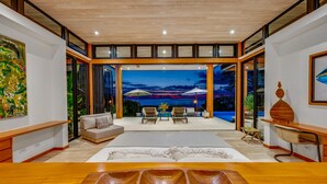 A modern interior with a wooden dining table, a sofa, and a view of a pool area at dusk. - Pacific Vistas Villa + Jungle View Casita - 2 Homes, Total Privacy, Mal Pais (Malpais)