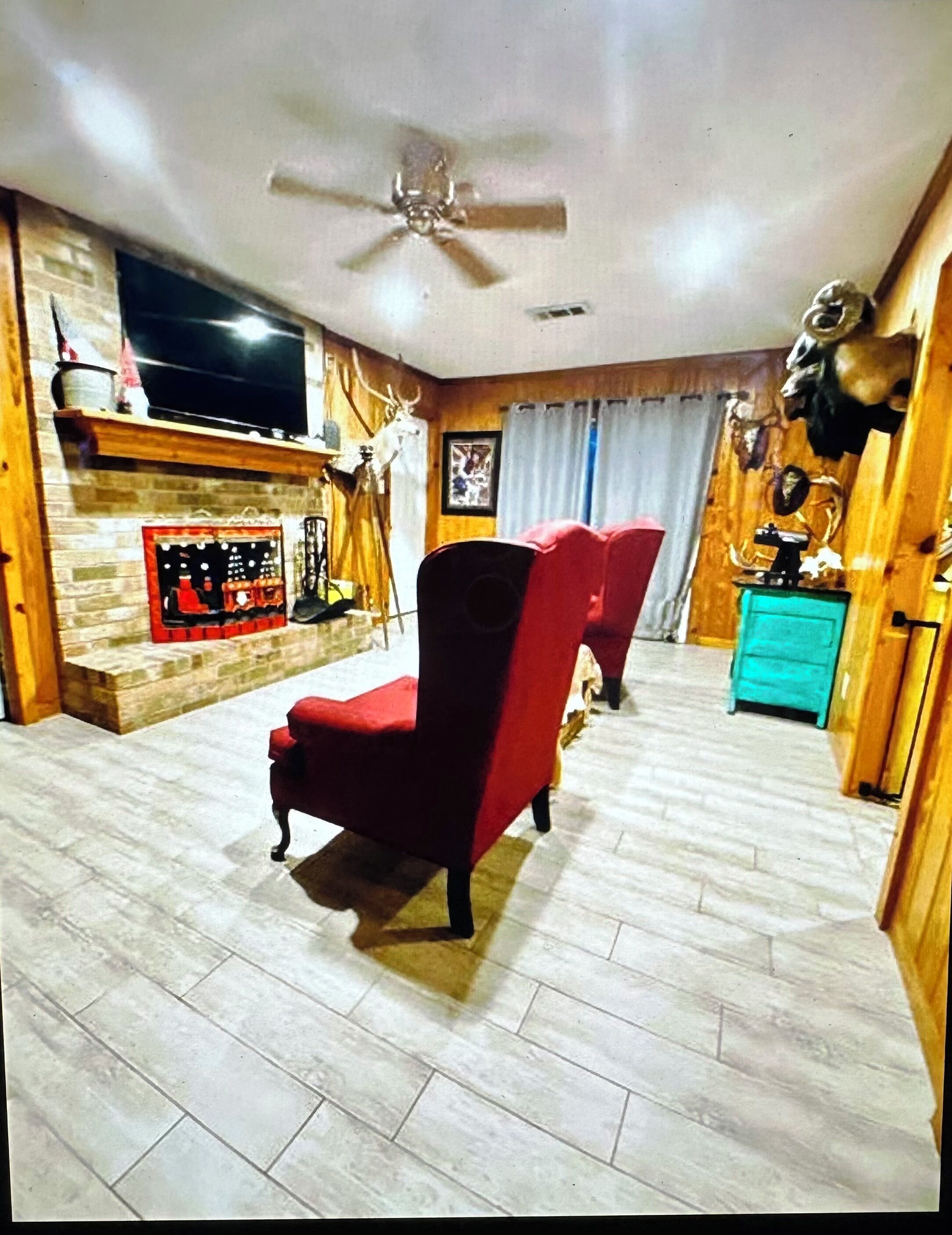 A living room with a red armchair, a ceiling fan, a fireplace, and a television.