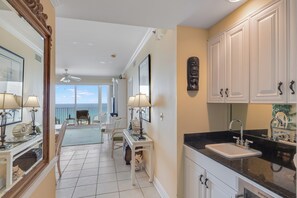 A hotel room with a balcony, a dining area, and a kitchen with white cabinets and a black countertop. - Princess Condos - All Units Are Gulf Front & Direct Beach Access in PCB! (Panama City Beach)