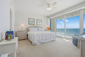 A bedroom with a large bed, two bedside tables, a ceiling fan, and a view of the ocean through large windows. - Princess Condos - All Units Are Gulf Front & Direct Beach Access in PCB! (Panama City Beach)