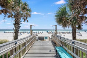 A wooden boardwalk leading to a beach with palm trees, beach chairs, and umbrellas. - Princess Condos - All Units Are Gulf Front & Direct Beach Access in PCB! (Panama City Beach)