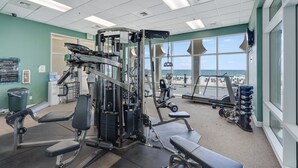 A gym with various exercise equipment, a water cooler, and a view of the beach through large windows. - Princess Condos - All Units Are Gulf Front & Direct Beach Access in PCB! (Panama City Beach)