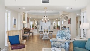 A spacious living room with a dining area, featuring a chandelier, wicker furniture, and a blue patterned sofa. - Beach & Gulf front Unit 1003 at Princess Condos 6415 Thomas Drive (Panama City Beach)