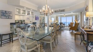 A spacious dining area with a glass table and white chairs, a chandelier, and a view of the ocean. - Beach & Gulf front Unit 1003 at Princess Condos 6415 Thomas Drive (Panama City Beach)