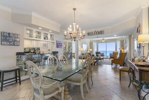 A spacious dining area with a glass table and white chairs, a chandelier, and a view of the ocean. - Beach & Gulf front Unit 1003 at Princess Condos 6415 Thomas Drive (Panama City Beach)