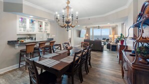 A spacious dining area with a long wooden table, multiple chairs, and a chandelier. - Princess Condos - All Units Are Gulf Front & Direct Beach Access in PCB! (Panama City Beach)