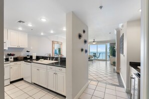 A modern kitchen with white cabinets, a black countertop, and a view to a balcony. - Princess Condos - All Units Are Gulf Front & Direct Beach Access in PCB! (Panama City Beach)