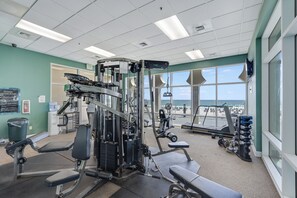 A gym with various exercise equipment, a water cooler, and a view of the beach through large windows. - Princess Condos - All Units Are Gulf Front & Direct Beach Access in PCB! (Panama City Beach)