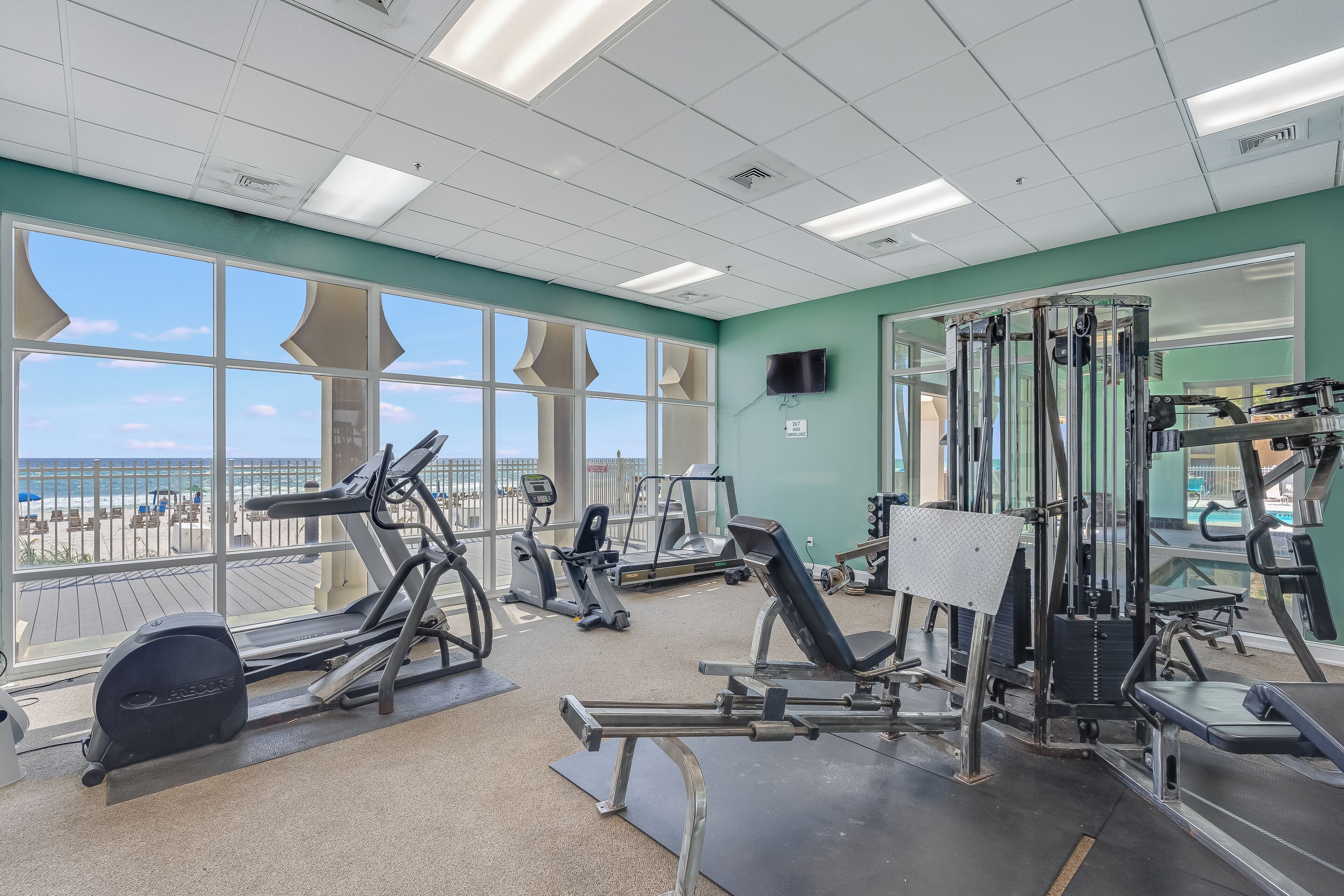 Un gimnasio con equipo de ejercicio, amplias ventanas y vistas a la playa.