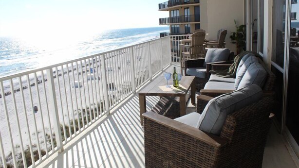Ein Balkon mit Korbmöbeln, einem Tisch mit einer Flasche und Blick aufs Meer.