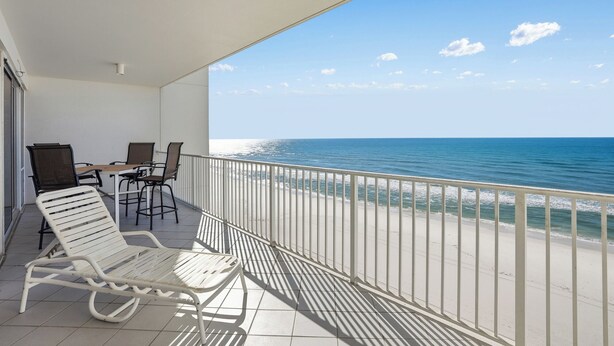 Un balcon avec vue sur l’océan, une chaise longue blanche et une table avec des chaises.