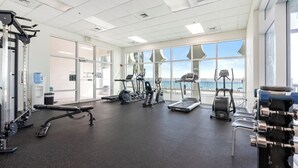A gym with cardio machines, weightlifting equipment, and large windows offering a view. - Princess Condos - All Units Are Gulf Front & Direct Beach Access in PCB! (Panama City Beach)